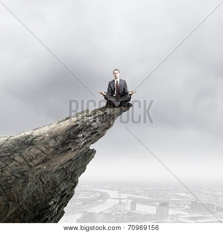 Young businessman sitting lotus pose on edge of rock mountain