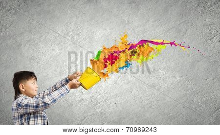 Young boy splashing colorful paint from bucket