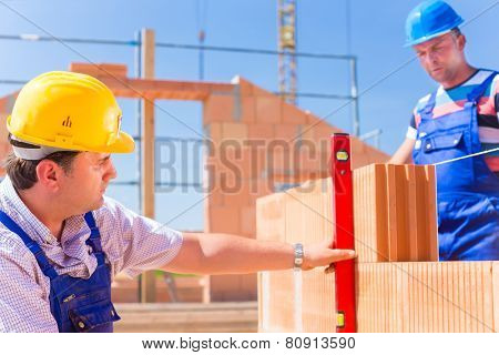 Construction site workers or bricklayer with helmets controlling building walls with a bubble level 