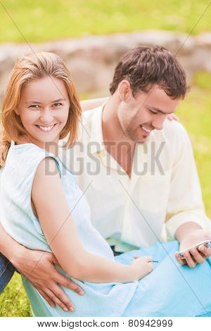 Happy Caucasian Couple Sitting Together Outdoors While Using Pda Handheld