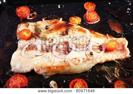 Dish of Pangasius fillet with onion and cherry tomatoes on burn pan background