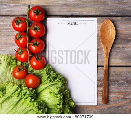 Menu sheet of paper with cherry tomatoes and lettuce on rustic wooden surface background