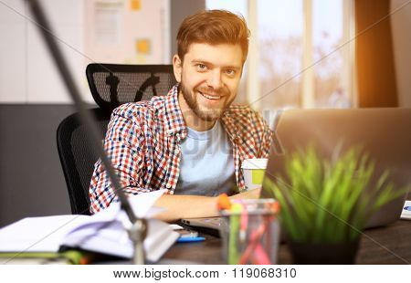 Enjoying good working day. Confident young man working on laptop while sitting at his working place