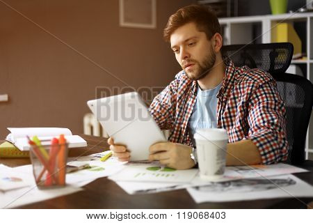 Thoughtful male person looking to the digital tablet screen while sitting in modern interior at the