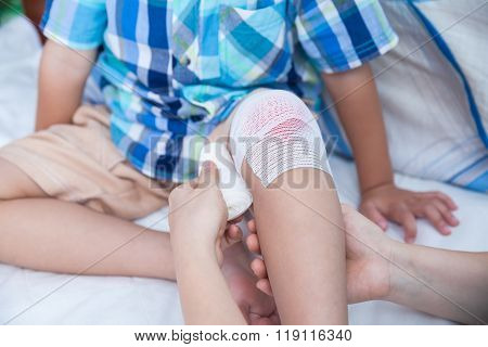 Child Injured. Mother Bandaging Son's Knee.
