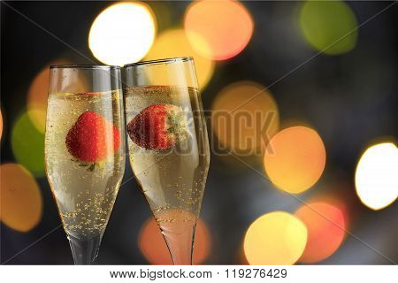 Closeup of stylish champagne flutes filled with chilled bubbly and a floating strawberries for celebrating a romantic evening together