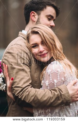 Stylish Loving wedding couple kissing and hugging in a pine forest near retro car