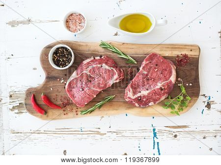 Raw fresh meat Ribeye steak entrecote and seasonings on cutting board over white wooden background.