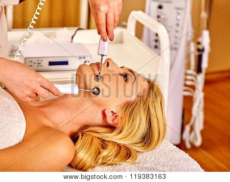 Young woman receiving electric galvanic face spa massage at modern beauty salon. 