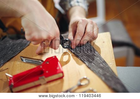 Removing ticks nail out of the board. Man upholstering chair in his workshop