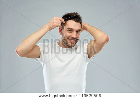 beauty, grooming and people concept - smiling young man brushing hair with comb over gray background