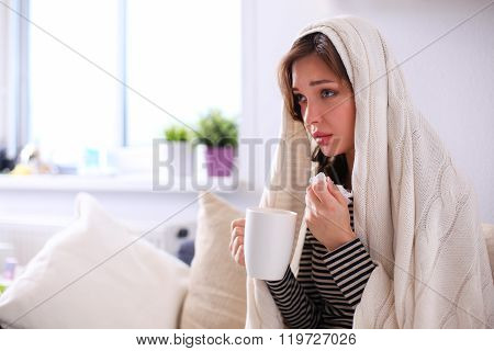 Portrait of a sick woman blowing her nose while sitting on the sofa