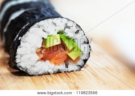 Sushi with salmon, avocado, rice in seaweed and chopsticks on wooden table. Japanese, Asian healthy food.