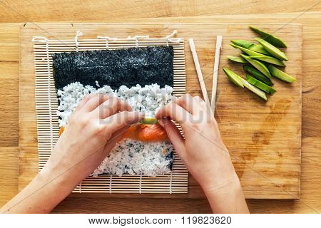 Preparing sushi. Salmon, avocado, rice on seaweed and chopsticks on wooden table. View from the top.