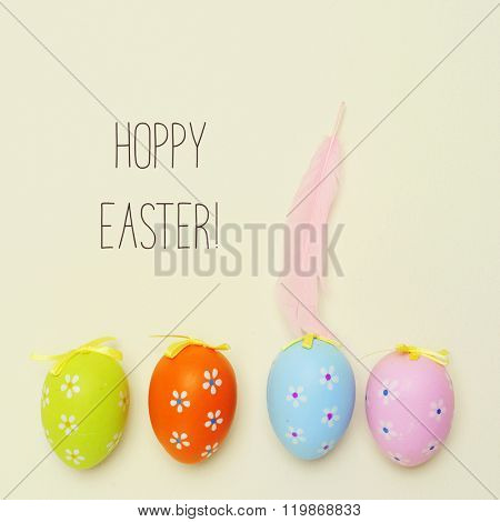 high-angle shot of some decorated easter eggs of different colors placed in line, a pink feather and the text hoppy easter