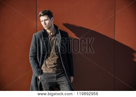 Young Man in a Winter Outfit Leaning on Red Wall