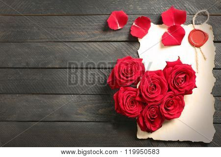 Fresh red roses buds in shape of heart with blank present card on wooden background
