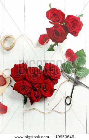 Fresh red roses buds in shape of heart with rope and scissors on wooden background