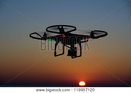 Flying drone with camera on the sky at sunset