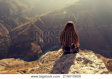 young girl sits with her back in the mountains