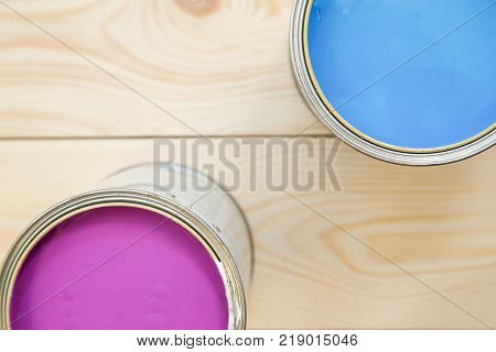 Painting a house. Tin cans of blue and fuchsia oil paint on a light uncolored wooden background. Close up. Top view. Space for your text or pruduct display.