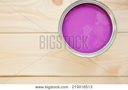 Painting walls. A tin can of fuschsia oil paint on a light uncolored wooden background. Close up. Top view. Space for your text or pruduct display.