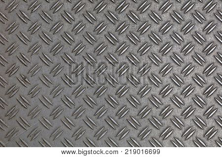 Dark gray industrial anti slip embossed metal steel plate with double diagonal bumps of diamond pattern texture background close up