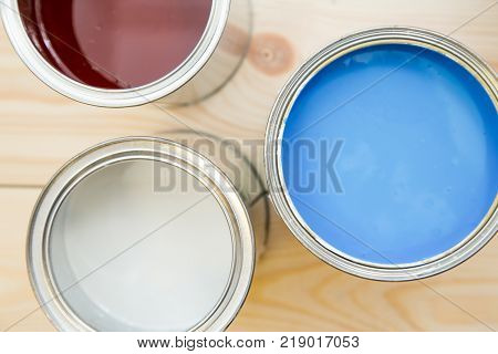 Painting new appartment. Tin cans of blue, white and brown, oil paint on a light uncolored wooden background. Close up. Top view. Space for your text or pruduct display.