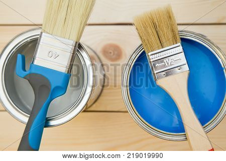 Ready to paint a house. Cans of household paint and brushes on a light uncolored wooden background. Close up. Top view. Space for your text or pruduct display.