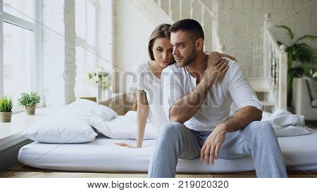 Depressed yong man sitting in bed having stressed while his girlfriend come and embrace him in bedroom at home