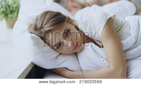 Depressed young woman lying in bed and feeeling upset after quarrel with her boylfriend in bedroom at home