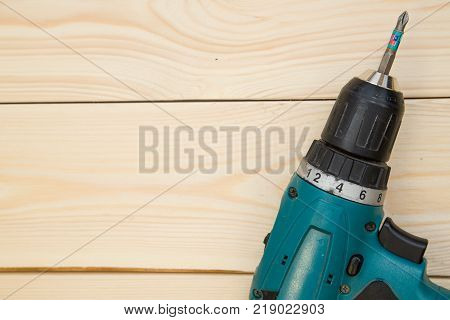 Repairing and construction concept. A screw gun on a light uncolored wooden background, close up. Top view. Space for your text or pruduct display.