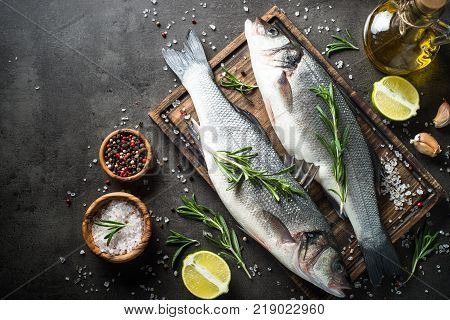 Fresh fish seabass. Raw fish seabass with spices and herbs on black slate background. Top view with copy space.