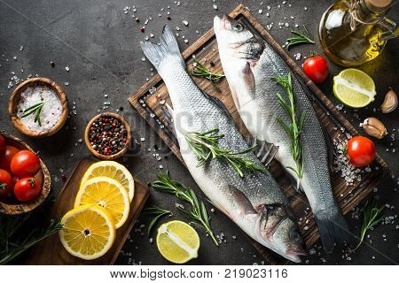 Fresh seabass. Raw fish seabass with spices and herbs on black slate table. Top view with copy space.