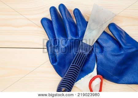 Repairing and construction concept. A plastering trowel and blue latex gloves on a light uncolored wooden background, close up. Top view. Space for your text or pruduct display.
