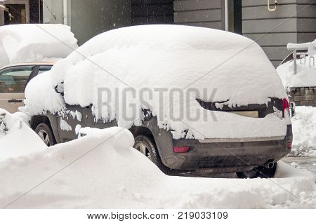 Car covered with first snow. Car buried under the snow and frozen. Bank of snow in winter