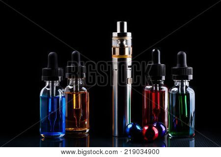 Electronic cigarette, bottles with assorted vape liquid and small colored christmas balls on black background