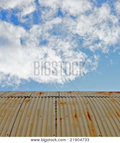 Viejo oxidado y soportó el techo de acero quonset hut contra un cielo azul con nubes de pelusa