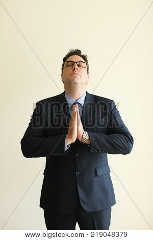 Meditative serene businessman trying to relax and keeping eyes closed. Contemplative male executive touching palms and praying. Hope concept