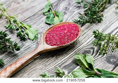 sumac seeds in a wooden spoon on rustic background. red seasoning
