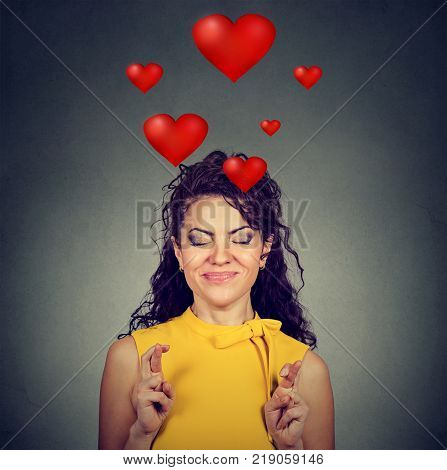 Young woman in love making a wish keeps her fingers crossed isolated on gray background