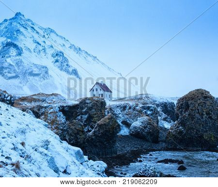 Lonely house behind cliffs near Arnarstapi village at dusk in winter, Snaefellsnes, Iceland.