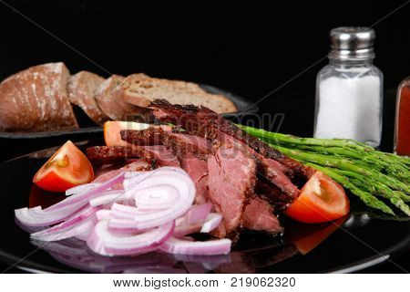 business lunch fresh roast beef meat slices on black plate wotj cutlery asparagus boiled broccoli rye bun on wooden table