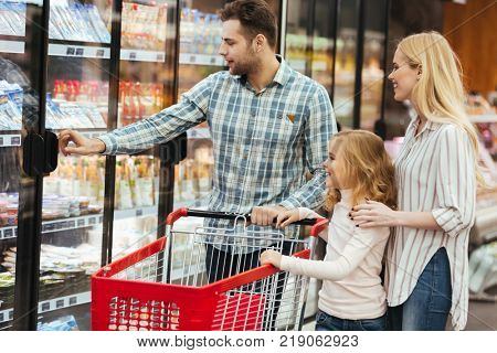 Happy family with child and shopping cart buying food at grocery store or supermark