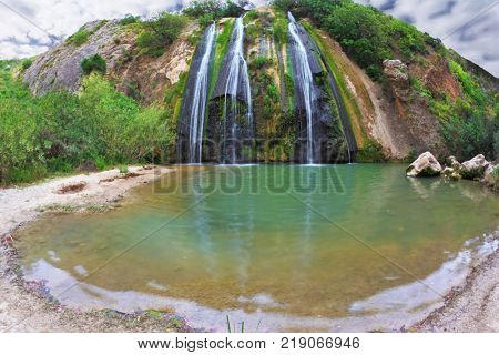 Three-jet scenic waterfall in the mountains. Three parallel streams of water running down the steep slope and fall in oval pool