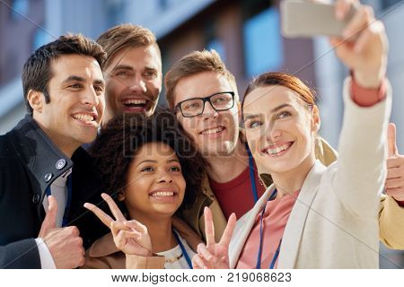 business, education and corporate concept - international group of people with smartphone taking selfie on city street and showing peace hand sign