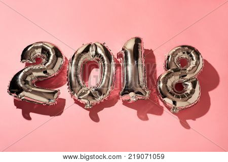 some silvery number-shaped balloons forming the number 2018, as the new year, against a pink background