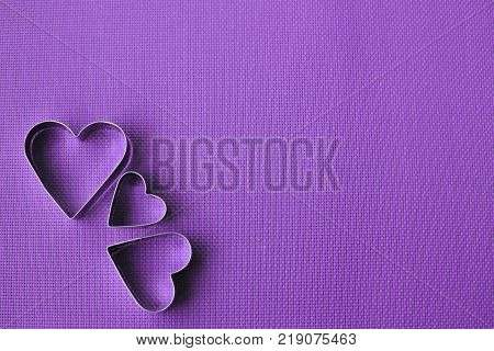 Three heart shaped cookie cutters over a purple background. Valentine's Day.
