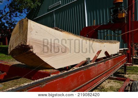 An old portable saw is cutting a tree log  and squaring it into dimensional lumber.