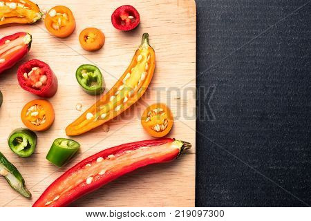 Colorful mix of chili pappers on wooden tray over black background. Free space for text